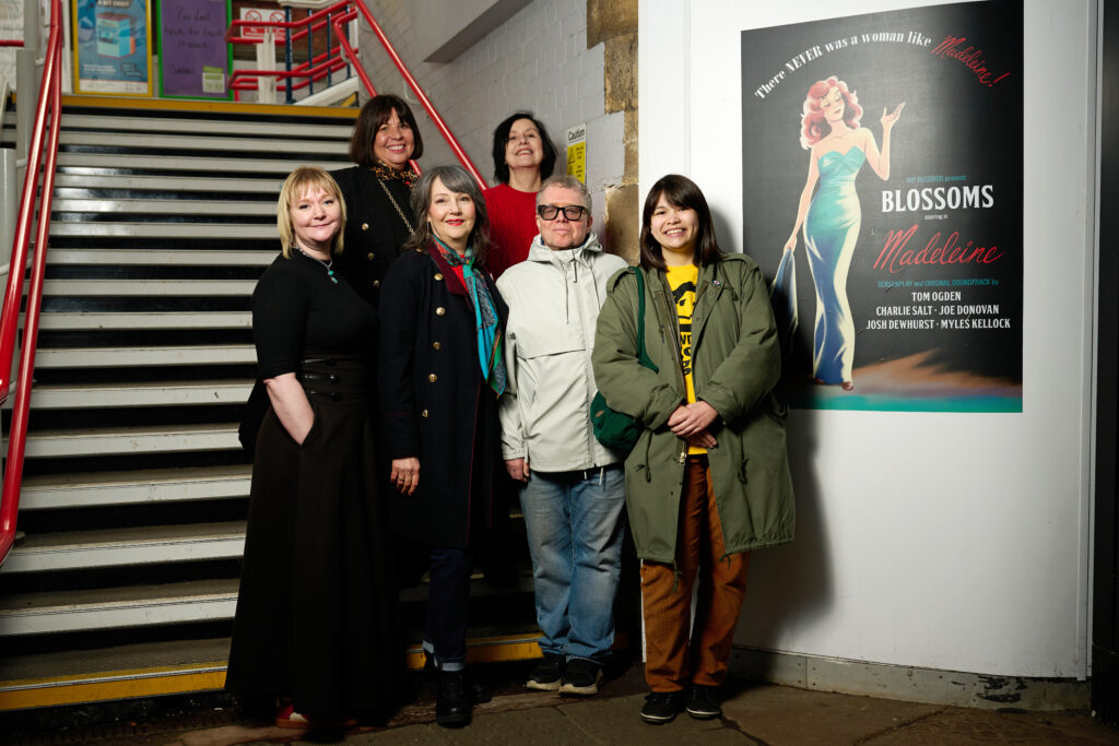 Group of people smiling and stood by music mural on wall.