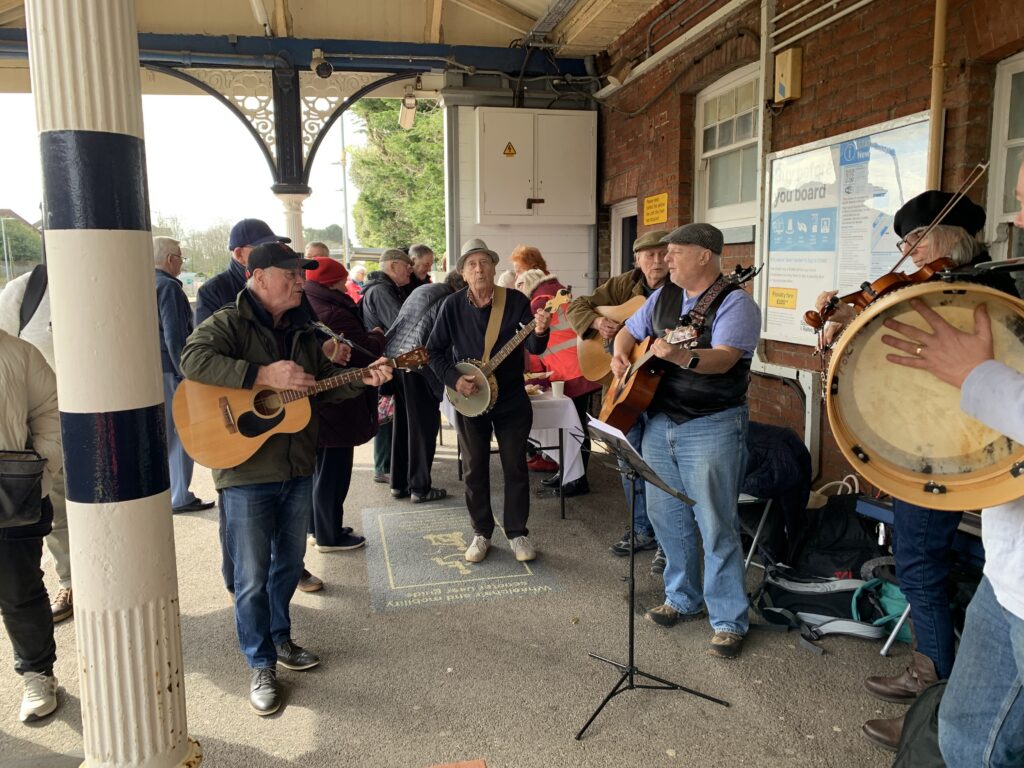People performing in a band on New Milton Station platform with a crowd of people around watching.
